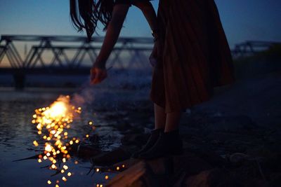 Low section of woman holding burning sparkler on lakeshore