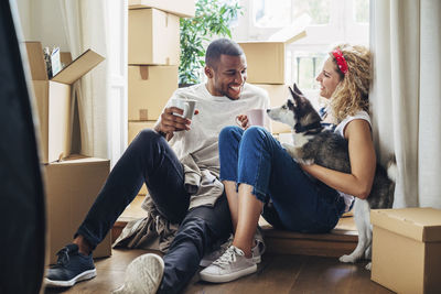 Happy couple playing with dog while sitting at doorway in new house