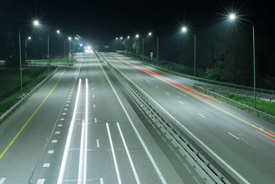 Country night track lit by lanterns. it shows streaks of light from the headlights of passing cars