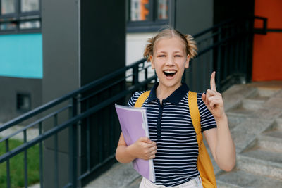 A teenage girl is standing at the stairs with her finger raised up, the girl came up with an idea