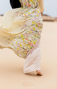 Low section of woman in traditional clothing walking on sand at beach