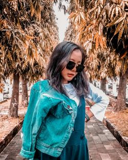 Young woman wearing sunglasses while standing on walkway against trees