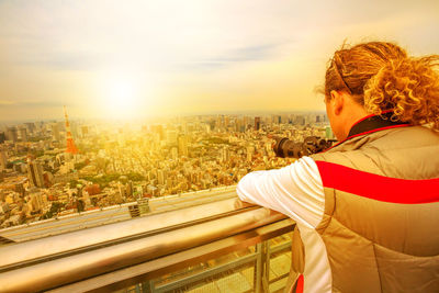 Man standing by railing photographing cityscape against sky