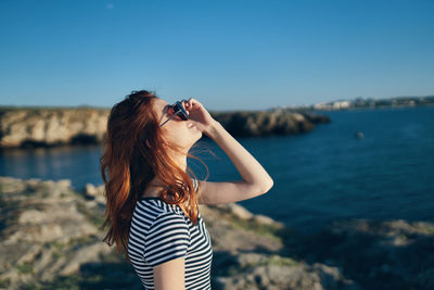 Woman wearing sunglasses standing by sea against sky