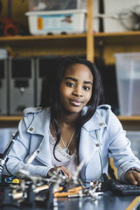 Portrait of smiling female high school student sitting with science project at desk in classroom