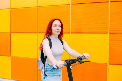 Young bright woman smiles and rides an electric scooter in the summer in city