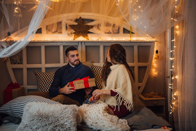 Young man giving christmas gift to woman on bed at home