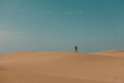 Man standing on sand dune in desert against sky