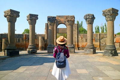 Rear view of woman standing by ancient columns against sky