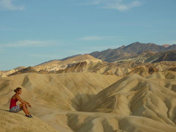 Full length of woman sitting on arid landscape against sky