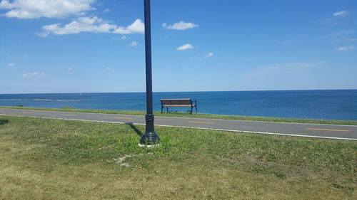 Grassy field by sea against blue sky