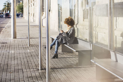 Woman using smart phone while sitting on seat at bus stop