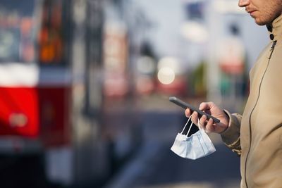 Midsection of man using smart phone standing by road