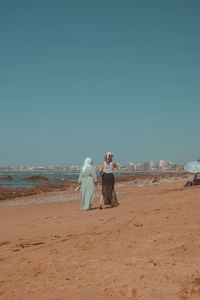 Rear view of couple on beach against clear sky