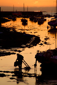 Men working on boat moored in sea against sky during sunset