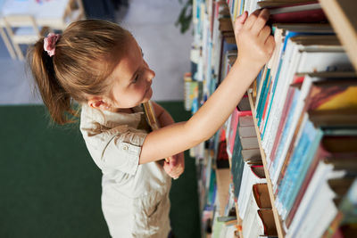 School girl looking at bookshelf in school library. smart girl selecting literature for reading