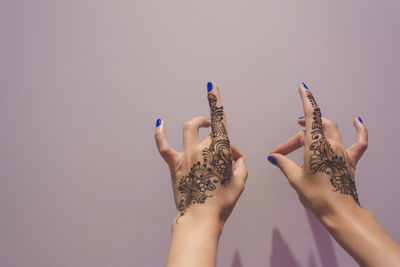 Cropped hands of woman with henna tattoo against purple background