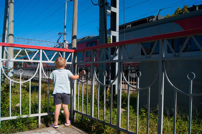 Rear view of boy looking at train while standing in balcony