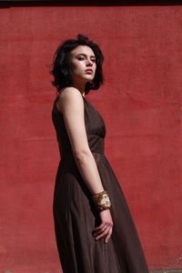 Beautiful woman in brown dress standing against red wall