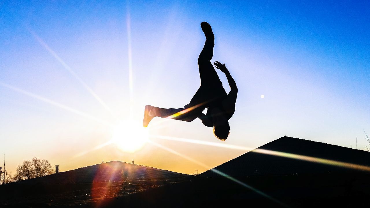 sun, lens flare, sunbeam, sunlight, jumping, one person, leisure activity, silhouette, sky, mid-air, real people, full length, lifestyles, sunset, motion, low angle view, outdoors, men, energetic, skill, clear sky, stunt, handstand, nature, day, extreme sports, flexibility, people