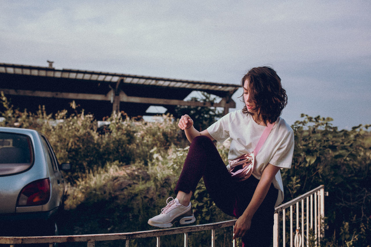 one person, real people, lifestyles, sky, leisure activity, casual clothing, young adult, mode of transportation, nature, motor vehicle, young women, transportation, car, sitting, adult, railing, day, focus on foreground, outdoors, hairstyle, contemplation