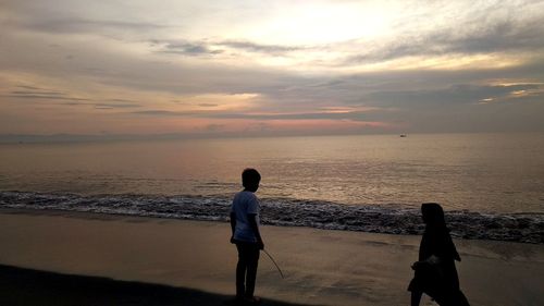 People on beach against sky during sunset