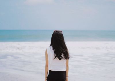 Rear view of woman standing at beach against sky