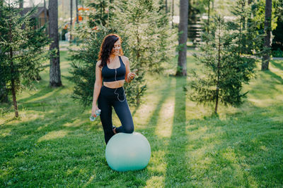 Woman using smart phone while standing by fitness ball in park