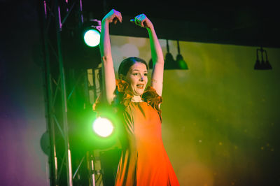 Portrait of young woman standing against illuminated lighting equipment at night