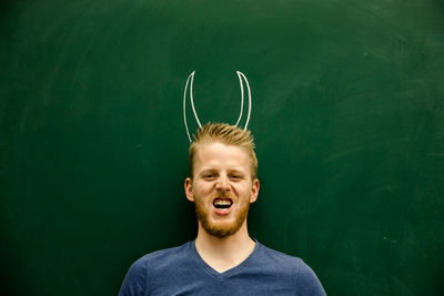 Portrait of young man with horned tattoo on blackboard