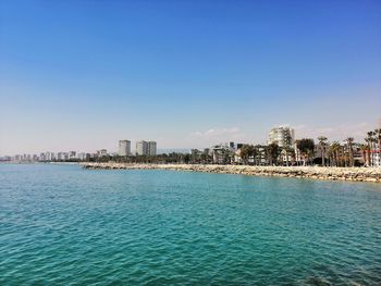 Sea by buildings against clear blue sky