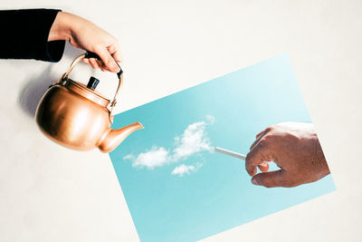 Optical illusion of hand holding tea kettle over photograph of man with cigarette emitting clouds