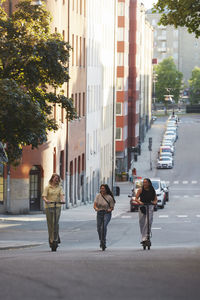 Young female friends riding electric push scooters in city