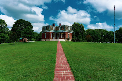 Lawn by building on field against sky