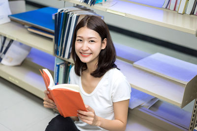 High angle portrait of young woman reading book while sitting in library