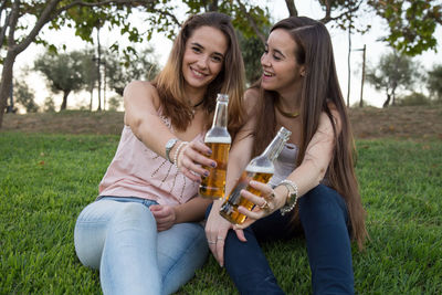 Happy friends enjoying beer while sitting on grass at park