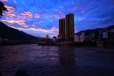 River by buildings against sky at sunset