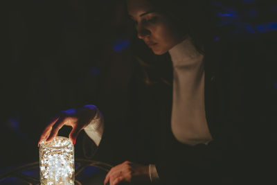 Woman holding jar with illuminated string light on table in darkroom