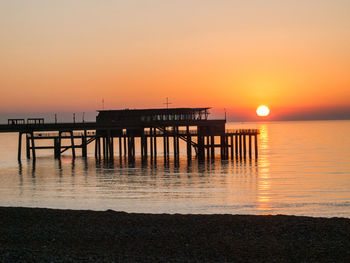 Pier over sea against orange sky