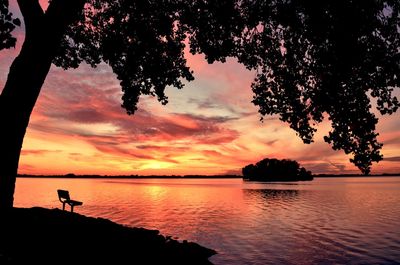 Silhouette trees by lake against cloudy orange sky during sunset