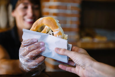 Smiling baker giving fresh pretzel to customer at counter in bakery