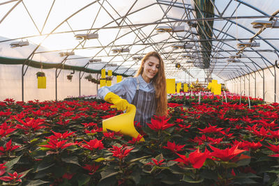 Smiling young woman watering plants while standing in greenhouse