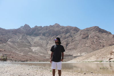 Rear view of man standing on mountain against clear sky