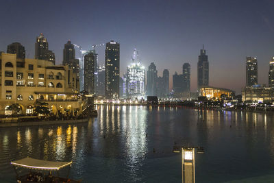 Illuminated buildings by river against sky in city at night