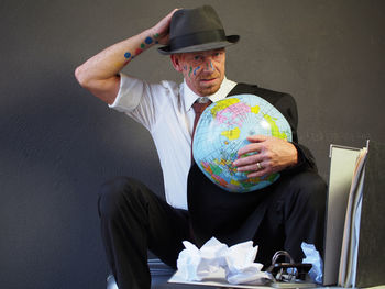 Portrait of businessman with face paint holding globe while standing at office