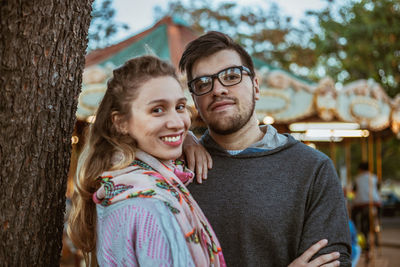 Portrait of smiling young couple standing by tree trunk