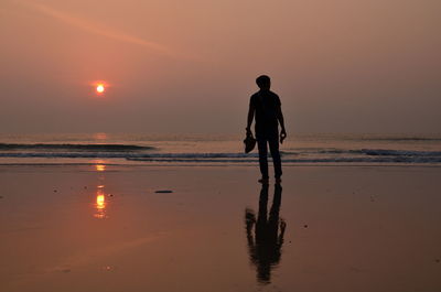 Rear view of man on beach against sky during sunset