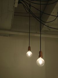 Low angle view of illuminated light bulbs hanging against wall