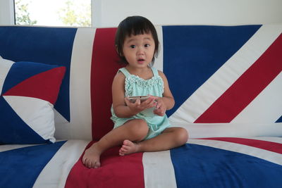 Full length portrait of cute girl sitting on sofa