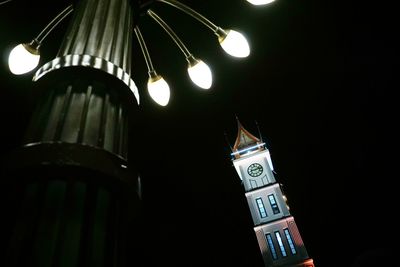 Low angle view of illuminated clock tower against building at night